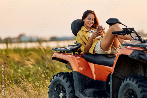 A smiling woman lying on a rented quad bike and using a mobile phone.