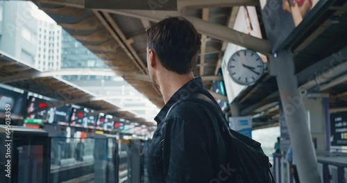 Young man in black shirt with backpack stands on the platform of the ground metro station, waiting for metro train. Caucasian male 30 waits for the train at the subway station public transport