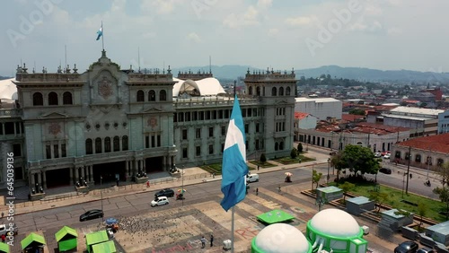 Bandera Guatemalteca ondenado al viento sobre asta en plaza municipal de la ciudad con palacio nacional de cultura de fondo  guatemala y la catedral metropolitana en el centro de la ciudad photo