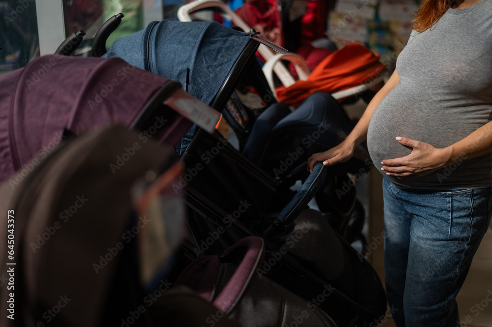 Faceless pregnant woman chooses a stroller in a children's store. Close-up of the abdomen.