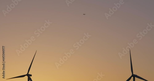Airplane passing overhead with wind turbines windmills spinning in the foreground against a sunset sky near Palm Springs California