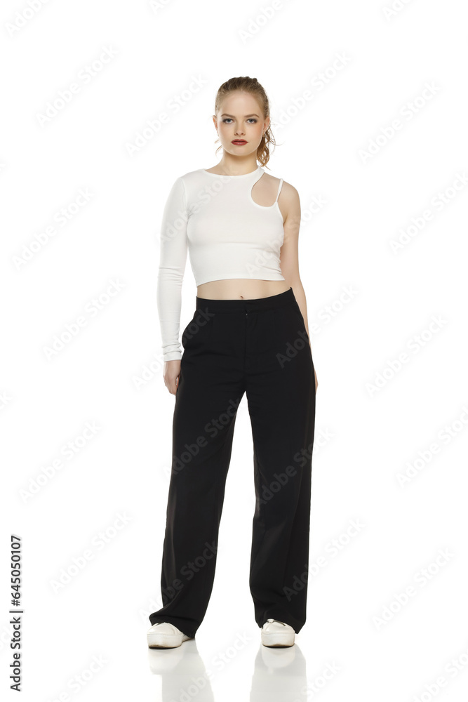 Front view of young blond woman in trousers and white blouse posing on white background
