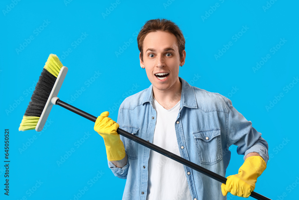 Surprised young man with broom on blue background Surprised young man with broom on blue background