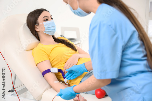 Female nurse taking blood from young donor in clinic