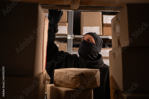Photography Thief in a black mask steals a box of parcel in a warehouse, close-up
