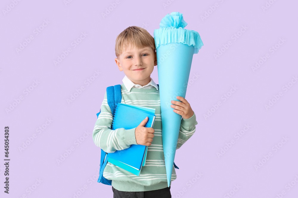 Happy little boy with backpack, blue school cone and notebooks on lilac background Happy little boy with backpack, blue school cone and notebooks on lilac background