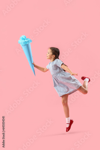 Happy little girl with blue school cone jumping on pink background
