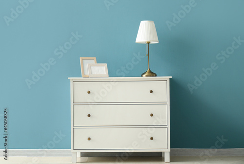 Blank picture frames and lamp on chest of drawers near color wall