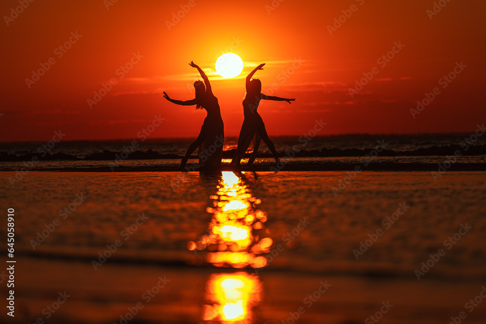 Silhouettes of dancing women against the backdrop of a red sunset on the seashore