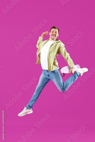 Happy jumping young man with skateboard on magenta background