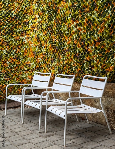 Fototapeta Naklejka Na Ścianę i Meble -  Secluded Oasis: 3 White Lounge Chairs in Gated Courtyard 🪑Discover maximum privacy with a special camouflage net as the backdrop.