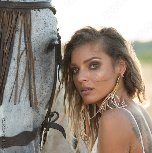 Beautiful blonde woman with curly hair with white hat and horse. Portrait of a girl with denim and her horse. Beautiful girl interacting and having fun with a horse at the ranch