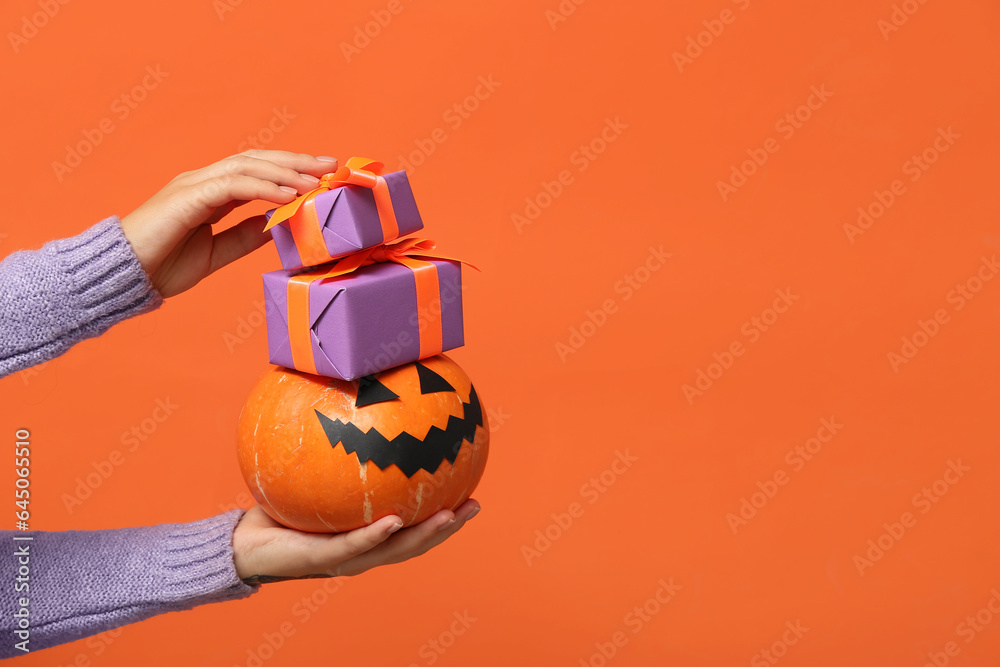 Female hands with gift boxes and Halloween pumpkin on orange background