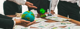 Businessman hand holding paper Earth with business people on meeting in office, planning and implementing eco-friendly ideal for corporate policy to reduce CO2 emission and save earth. Trailblazing