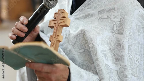  An Orthodox priest in a white cassock reads the Bible in a church and holds a wooden cross in his hands. Church liturgy. photo