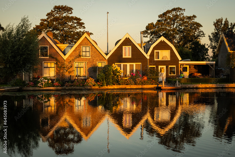 Fototapeta premium Traditional style Dutch architecture houses reflecting off the still water of the Oude Rijn river in the morning golden hour. riverside lifestyle with natural beauty for living comfort