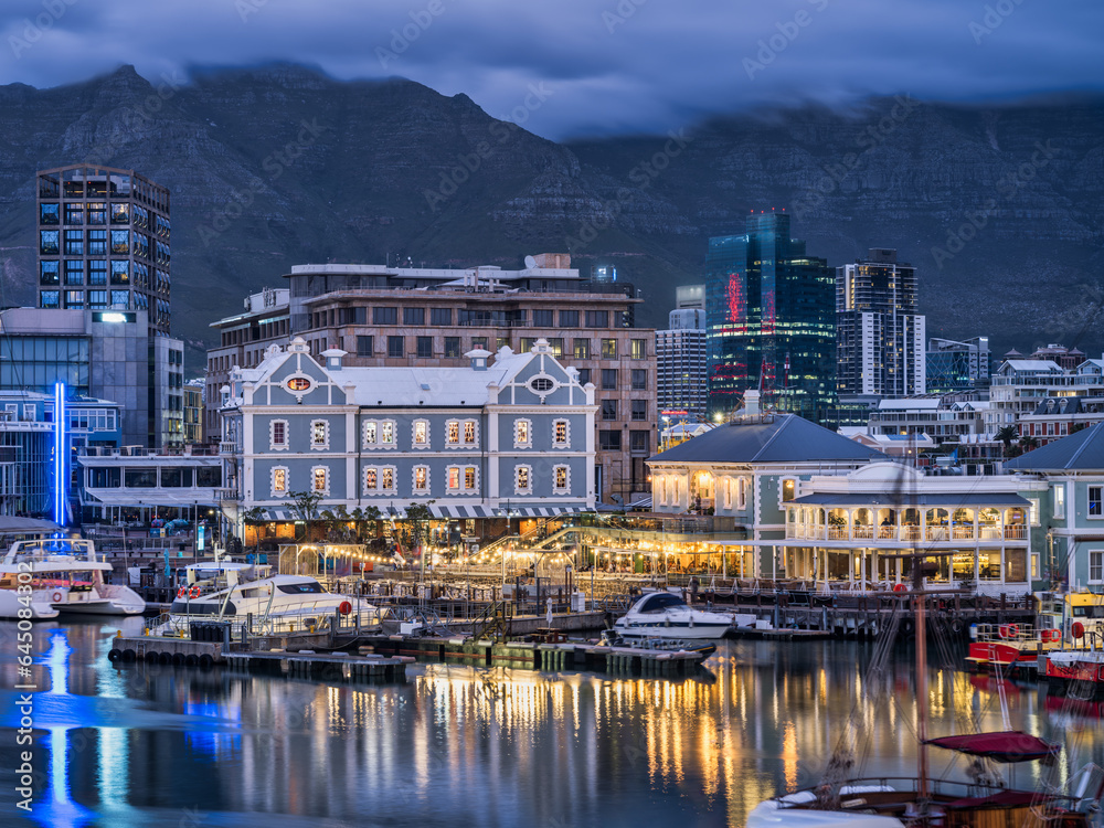 V and A Waterfront lit up with the table mountain in the background during a cloudy evening, Cape Town, South Africa