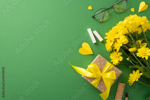 Teacher\'s Day inspiration: Top view of chrysanthemums, gift box, chalk, glasses, paper hearts, pencil, ruler on a green blackboard. Empty area for text or advertisements