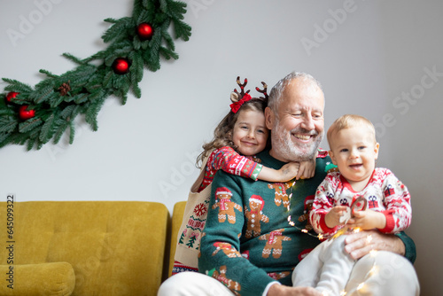 Grey haired mature father with two little children celebrating Christmas and having fun at home 