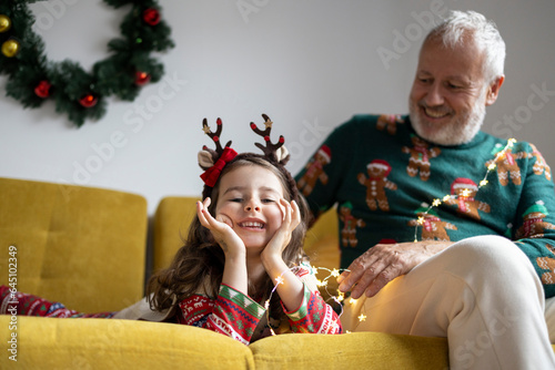 Grey haired mature man and a little girl in Christmas sweater having fun and celebrating Christmas at home 
