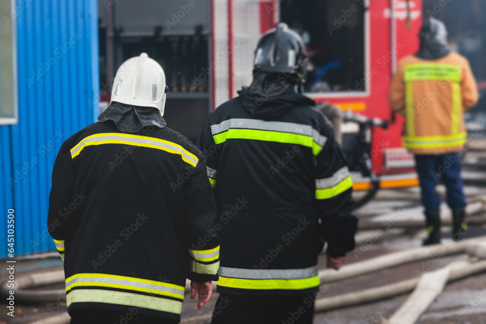 Group of fire men in protective uniform during fire fighting operation in the city streets, firefighters brigade with the fire engine truck vehicle in the background, emergency and rescue service Group of fire men in protective uniform during fire fighting operation in the city streets, firefighters brigade with the fire engine truck vehicle in the background, emergency and rescue service