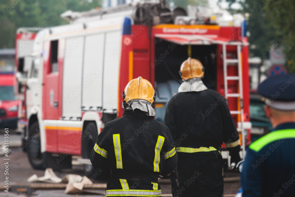 Group of fire men in protective uniform during fire fighting operation in the city streets, firefighters brigade with the fire engine truck vehicle in the background, emergency and rescue service Group of fire men in protective uniform during fire fighting operation in the city streets, firefighters brigade with the fire engine truck vehicle in the background, emergency and rescue service