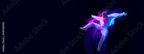 Young muscular man in white stylish clothes jumping on black studio background in neon with mixed lights effect. Concept of movements, art, dance and sport, fashion, youth. Banner. Copy space for ad