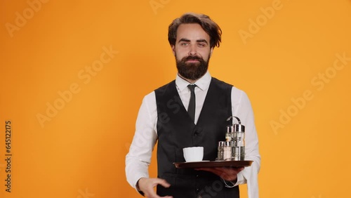 Elegant butler having new idea on camera, raising index finger and indicating upwards direction with restaurant food tray in hand. Skilled waiter feeling genious, innovative with fresh thoughts.