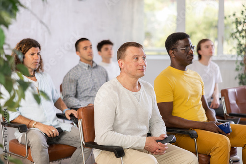 Portrait of attentive positive adult male student attending training session in lecture class with group of men in college © JackF