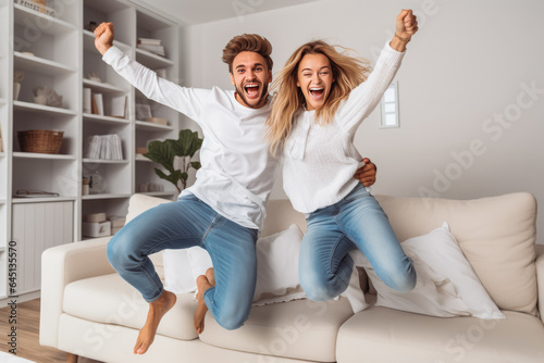 Beautiful young energetic caucasian couple jumping off sofa in the living room and smiling, young love