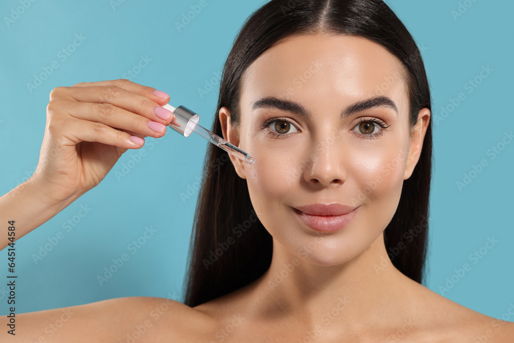 Beautiful young woman applying serum onto her face on light blue background Beautiful young woman applying serum onto her face on light blue background