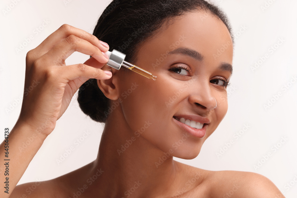 Smiling woman applying serum onto her face on white background, closeup