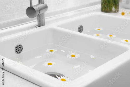 Sink with water and beautiful chamomiles indoors
