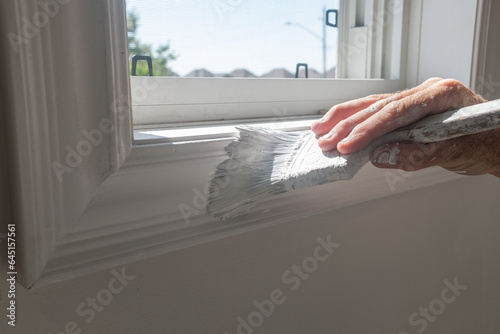 Painter painting the bottom of a window frame with white paint and an angled sash brush with  close up of hand