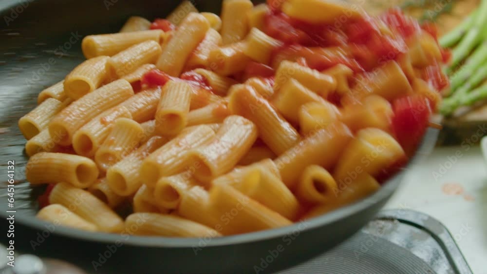 Tossing rigatoni with tomato sauce in a skillet while cooking delicious pasta. Extreme close-up shot in slow mo Tossing rigatoni with tomato sauce in a skillet while cooking delicious pasta. Extreme close-up shot in slow mo
