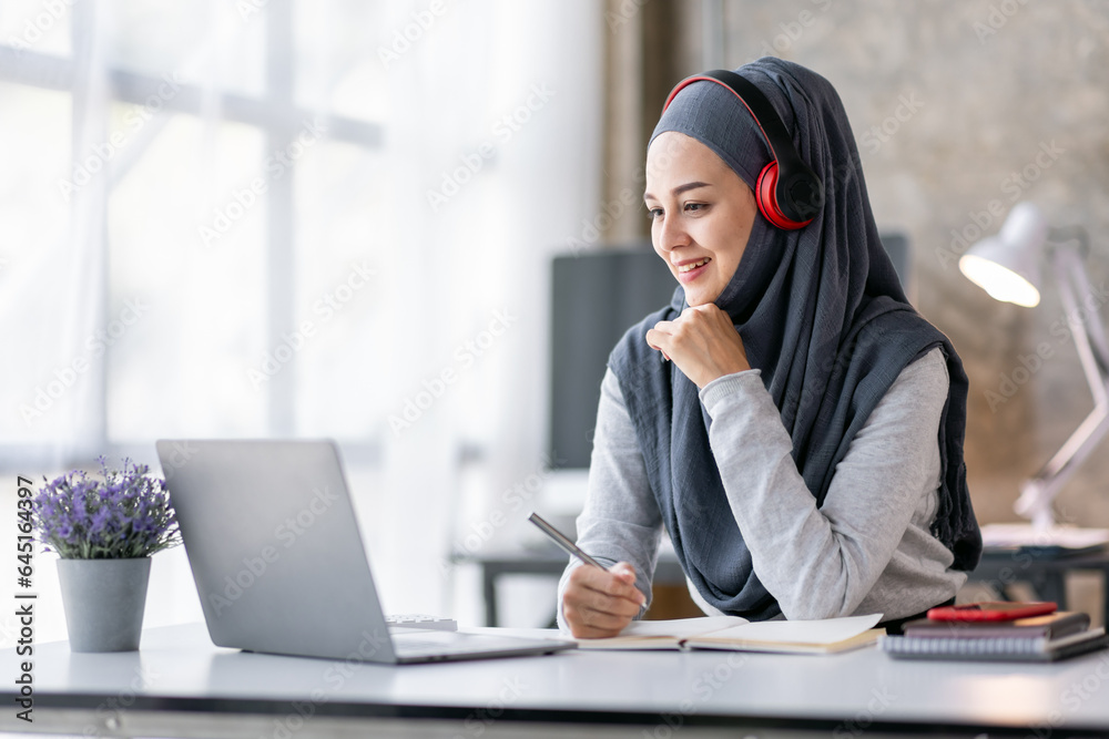 Online Education For Muslim Asian Women. Happy Arabic Girl In Headscarf And Headset Studying With Laptop At Home, Taking Notes While Watching Webinar Online Education For Muslim Asian Women. Happy Arabic Girl In Headscarf And Headset Studying With Laptop At Home, Taking Notes While Watching Webinar