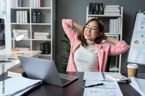 Young Asian businesswoman relaxing from work, drinking hot coffee, stretching after sitting at desk for a long time, fatigue. Office syndrome concept.
