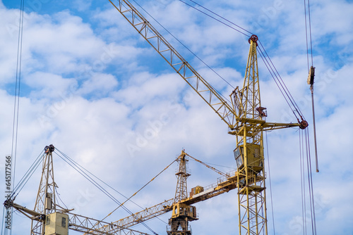 A crane and a building under construction against a blue sky background. Builders work on large construction sites, and there are many cranes working in the field of new construction.