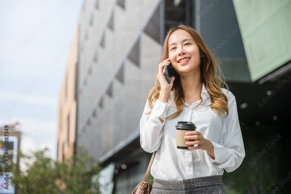 Asian young businesswoman walking outdoors talking on cell smart mobile phone and holding coffee cup takeaway, lifestyle business woman hold paper cup and calling smartphone outside office