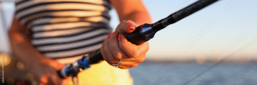 Woman is holding fishing rod while standing on boat, sea is in background.