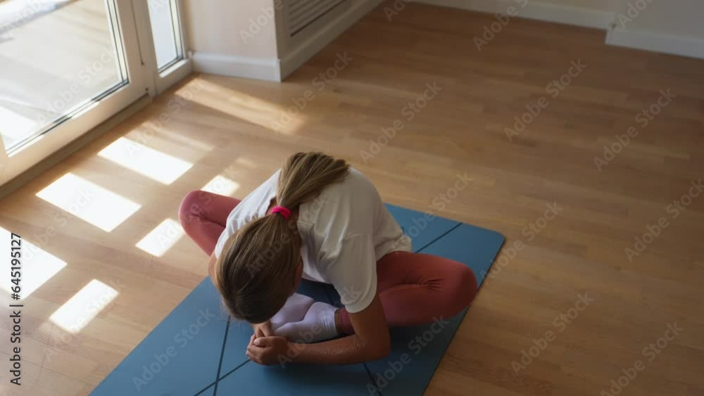 Top view of flexible preteen girl sitting butterfly pose bending forward during yoga home workout., in sunny living room by window. Concept of exercises for children at home and healthy lifestyle Stock ビデオ | Adobe Stock
