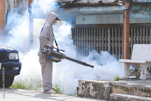 Healthcare worker in protective clothing on street is spraying chemical to eliminate mosquitoes in overgrown area at abandoned house in outdoors public area