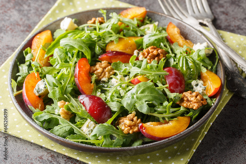 Homemade plum salad with arugula, gorgonzola cheese and walnuts close-up in a plate on the table. horizontal