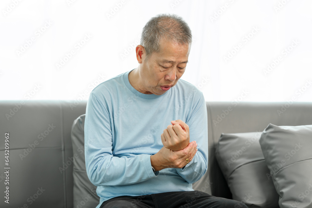 Elderly Asian gentleman with wrist discomfort on the couch, expressing pain due to Carpal Tunnel Syndrome. Elderly Asian gentleman with wrist discomfort on the couch, expressing pain due to Carpal Tunnel Syndrome.