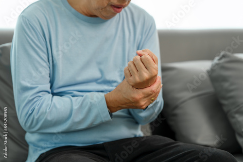 Canvastavla Elderly Asian gentleman with wrist discomfort on the couch, expressing pain due to Carpal Tunnel Syndrome