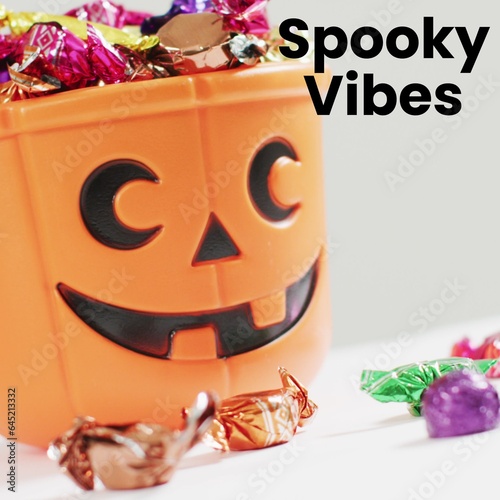 Composite of spooky vibes text and halloween pumpkin with sweets on white background