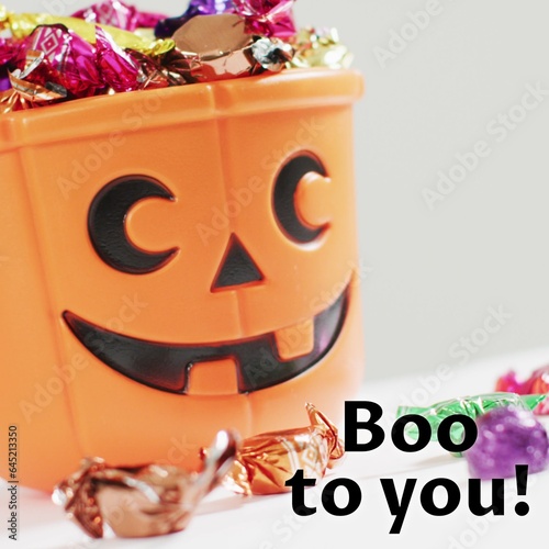 Composite of boo to you text and halloween pumpkin bucket and sweets on white background