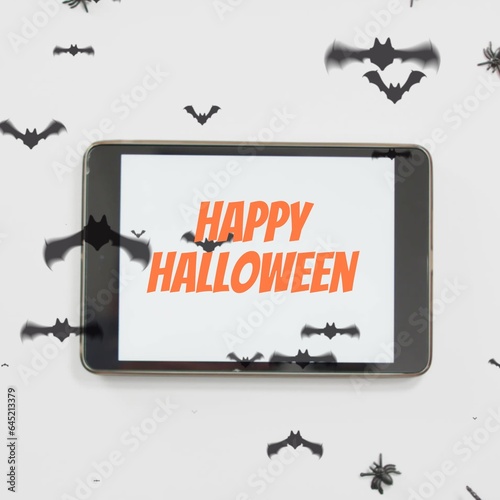 Composite of happy halloween text on tablet and halloween bats on white background