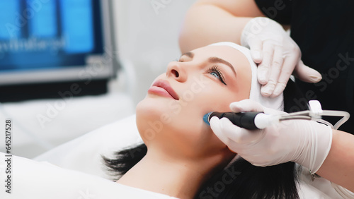 Cosmetologist doing hydrafacial treatment on woman face in beauty clinic photo