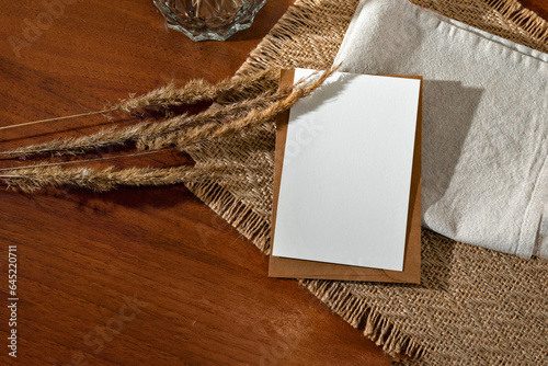 Blank paper card mock up, envelope, and meadow grass on wooden table background with linen and jute napkins. Boho natural wedding invitation template, business brand flat lay